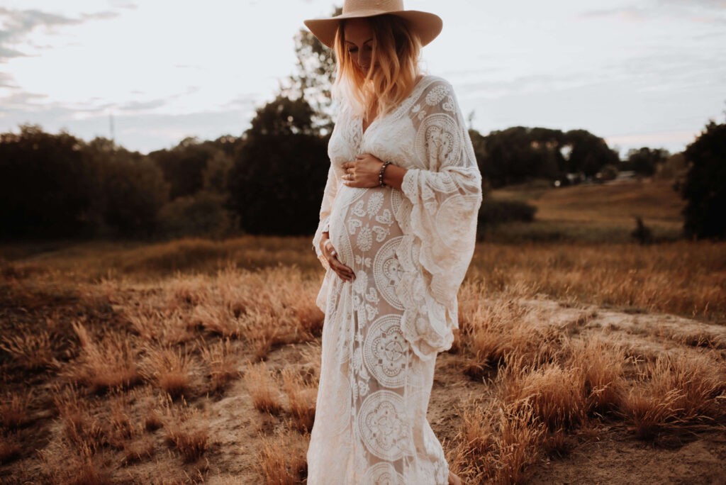 Schwangere trägt Spitzenkimono und Hut in der Natur, hält Babybauch
